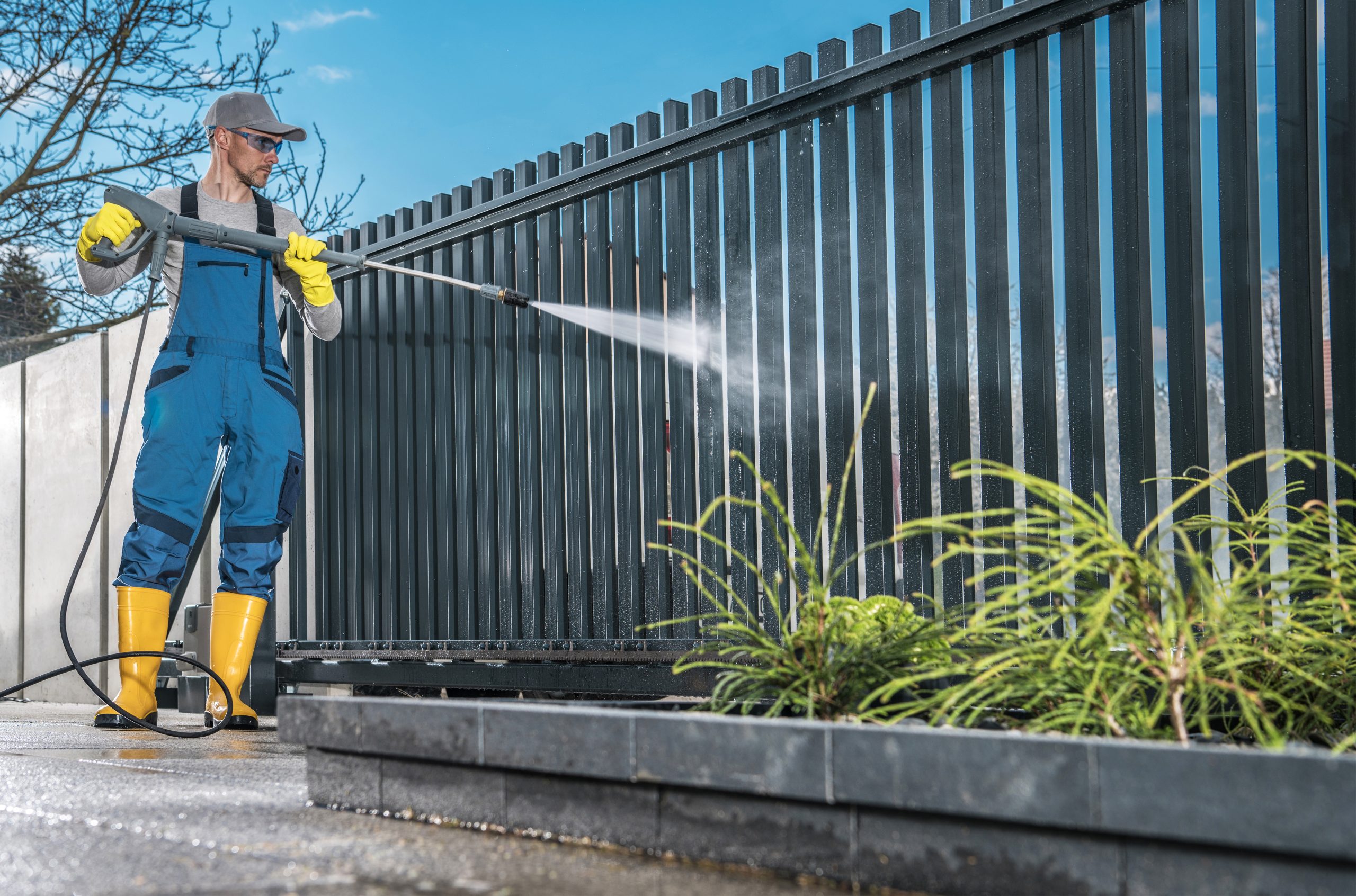 Caucasian Men Washing His Residential Driveway Gate Using Pressure Washer. Home Surrounding Maintenance.
