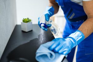 Person with gloves spraying and wiping down a table